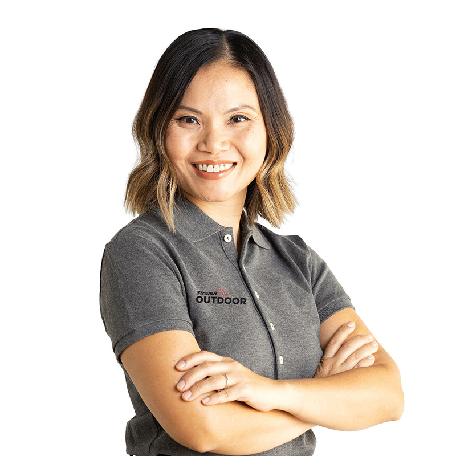 A smiling woman in a grey polo shirt stands with arms folded