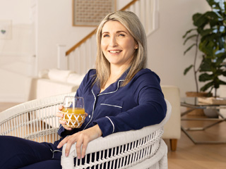 A smiling woman in navy pyjamas enjoys a morning drink on the patio